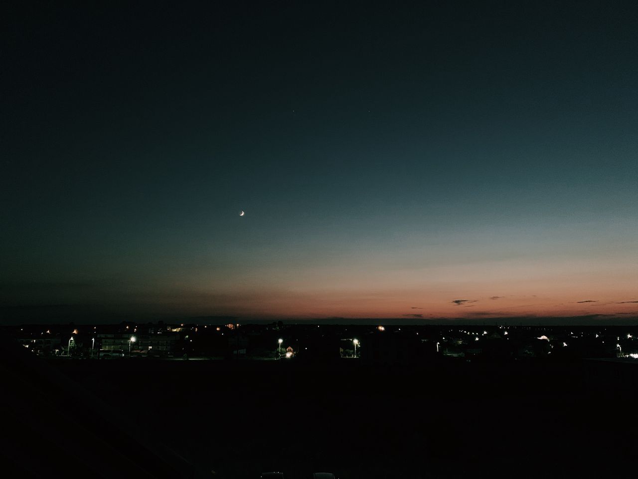 Services Starless dark sky with new moon glowing over small settlement houses illuminated by electric lights