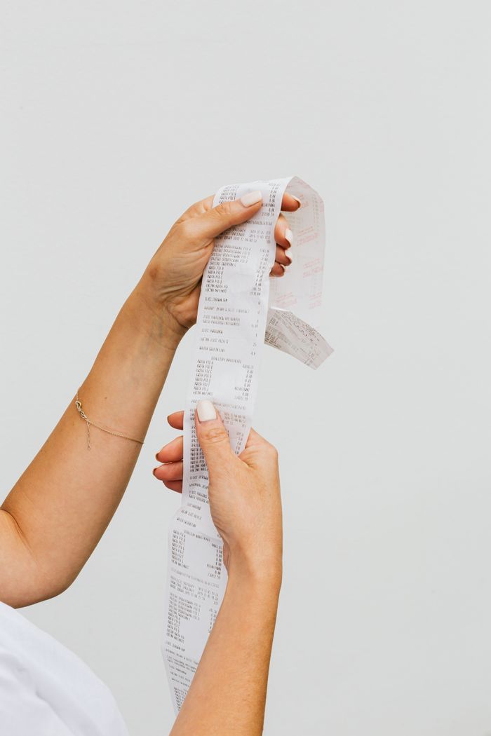 fitness-service-01 Close-up of woman's hands holding a long receipt against a white background, representing shopping or budgeting.